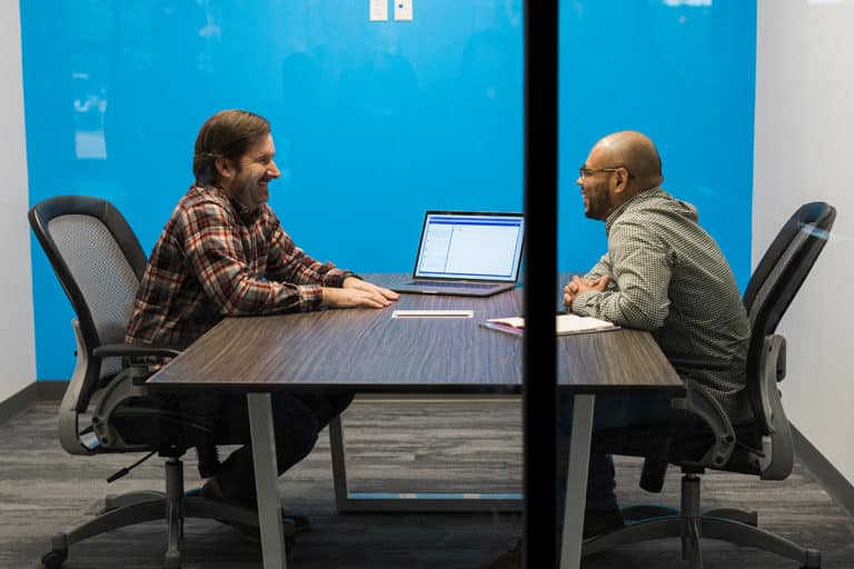 two men sitting at desk in meeting room laughing